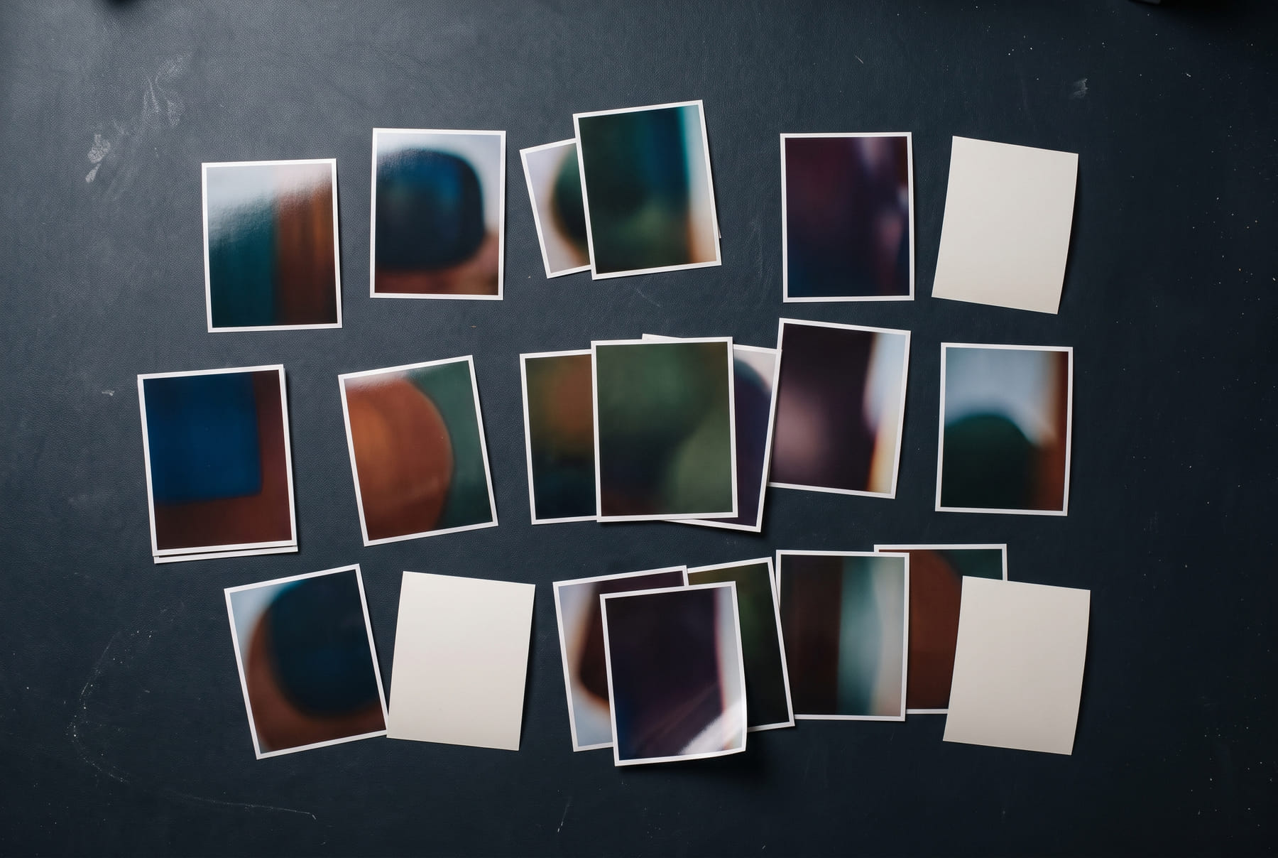 FIG.01 — twenty small glossy concept prints scattered on a black desk, all sharing one deep palette and agreeing on nothing else, several lying face-down