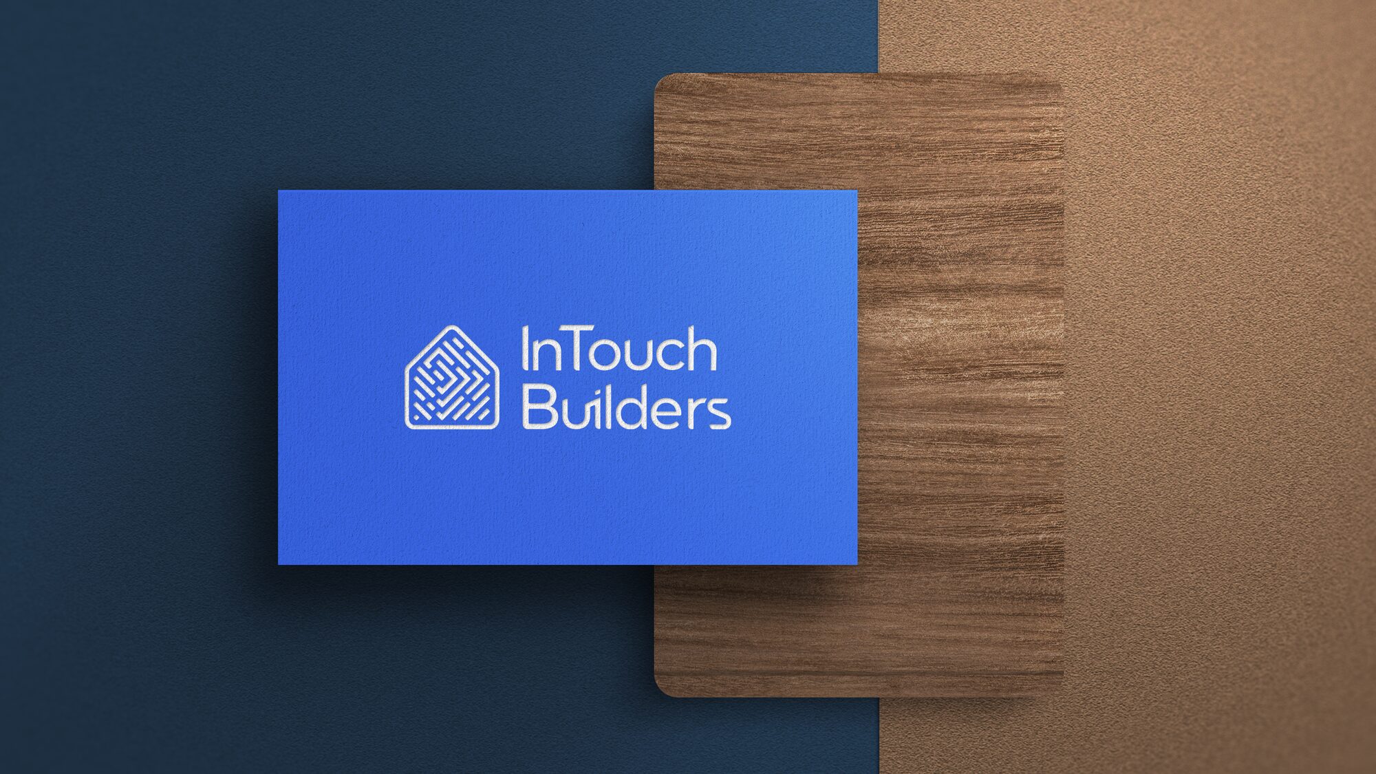FIG.08 — the InTouch Builders business card in Mediterranean Blue, laid over a timber board on a navy ground