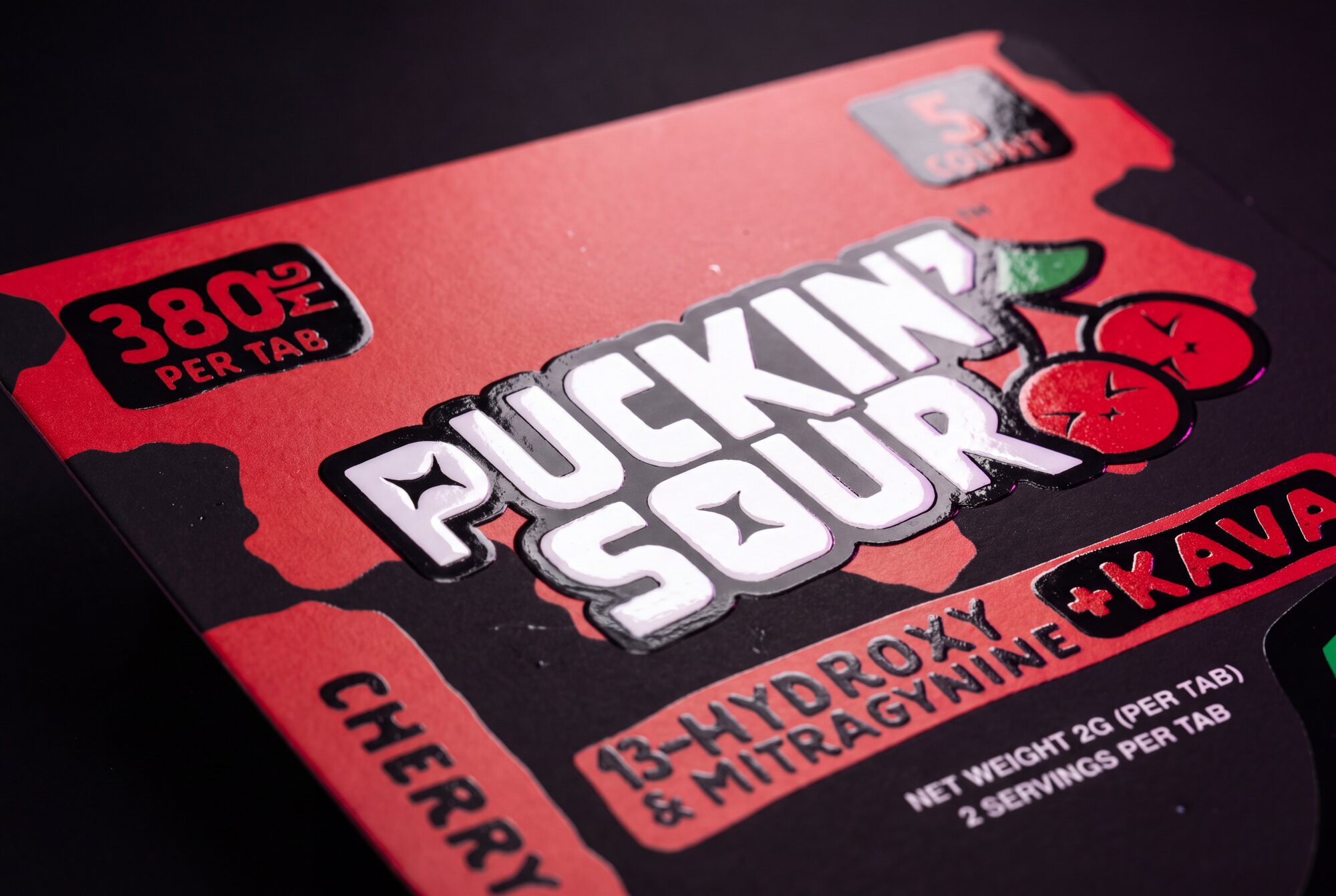 FIG.08 — macro of the Cherry Bombs card under raking light, spot gloss standing proud of the matte board